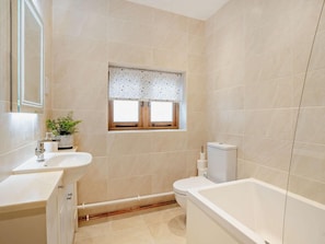 Ein Badezimmer mit Badewanne, Toilette, Waschbecken und einem Fenster mit gemustertem Rollo.