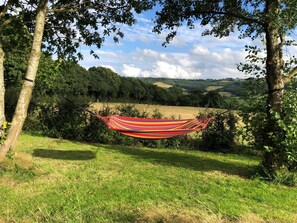 A hammock strung between trees in a grassy area with a view of rolling hills and a partly cloudy sky. - 1 Bed in Chepstow (oc-91941) (Chepstow)