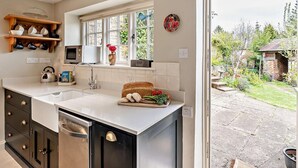 A kitchen with a large window, a dishwasher, and a wooden shelf with dishes. - 2 Bed in Banbury (oc-92008) (Hook Norton)