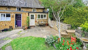 A stone cottage with a thatched roof, a small garden with tulips, and a paved patio area. - 2 Bed in Banbury (oc-92008) (Hook Norton)