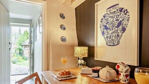 A dining area with a wooden table, plates of food, a glass of juice, a lamp, and a framed artwork on the wall. - 2 Bed in Banbury (oc-92008) (Hook Norton)