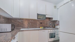 A kitchen with white cabinets, a granite countertop, a microwave, a sink, an oven, and a refrigerator. - 2-bedroom apartment • St. Paul's Basilica • Metro B, 600 meters • A/C (Roma)