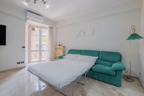 A room with a bed, a green sofa, a floor lamp, and a wall-mounted air conditioner. - 2-bedroom apartment • St. Paul's Basilica • Metro B, 600 meters • A/C (Roma)