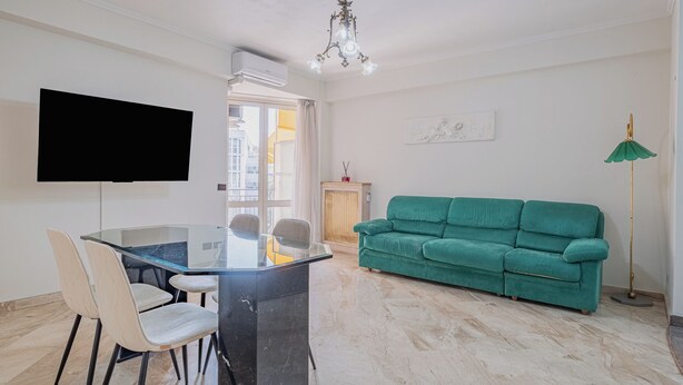 A living room with a green sofa, a dining table with chairs, a flat-screen TV, a chandelier, and a floor lamp. - 2-bedroom apartment • St. Paul's Basilica • Metro B, 600 meters • A/C (Roma)