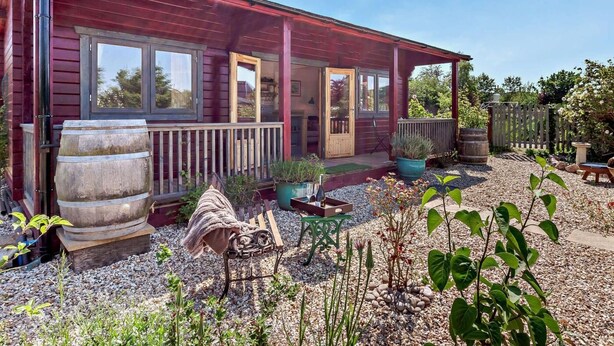 A rustic cabin with a covered porch, large windows, and a gravel yard with potted plants. - 1 Bed in Bristol (oc-91933) (Claverham)
