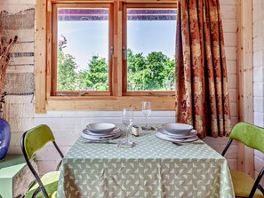 A dining area with a table set for two, a window with curtains, and a view of greenery outside.