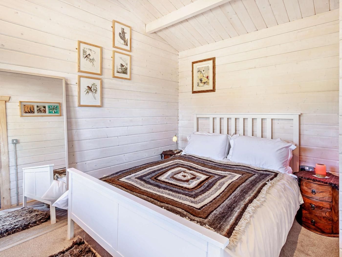 A bedroom with a white bed, a patterned rug, and framed artwork on the wall.