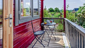 A wooden deck with a red railing, a small table with chairs, and a window overlooking a garden. - 1 Bed in Bristol (oc-91933) (Claverham)