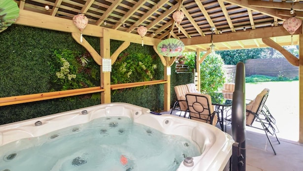 Un bain à remous sous une pergola en bois, avec un mur végétal en arrière-plan et des meubles d’extérieur.