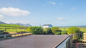A flat-roofed building with a white exterior, surrounded by green fields and mountains in the distance. - 2 Bed in Caernarfon (oc-92082) (Aberdesach)