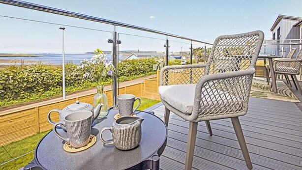Un balcón con sillas de mimbre, una mesa con juego de té y vista al mar.