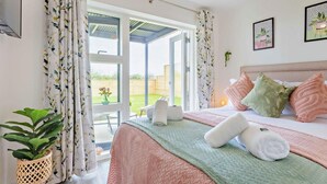 Un dormitorio con cama, almohadas, una mesita de noche, una planta y vistas al exterior.