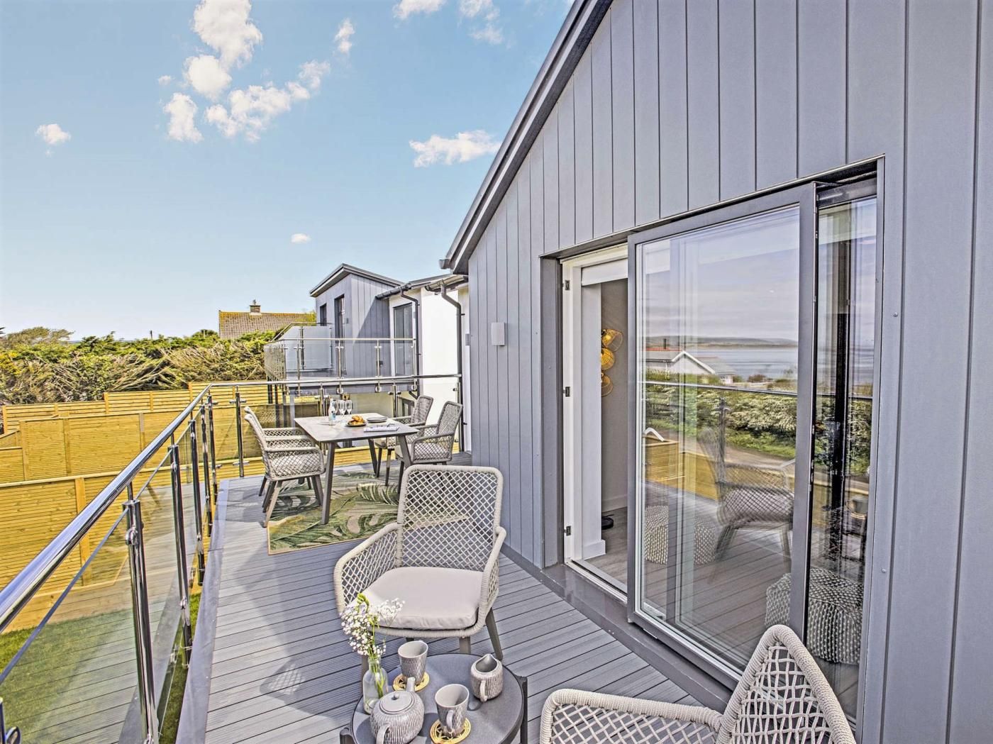 A modern outdoor deck with a table set for two, surrounded by wicker chairs, overlooking a scenic landscape.