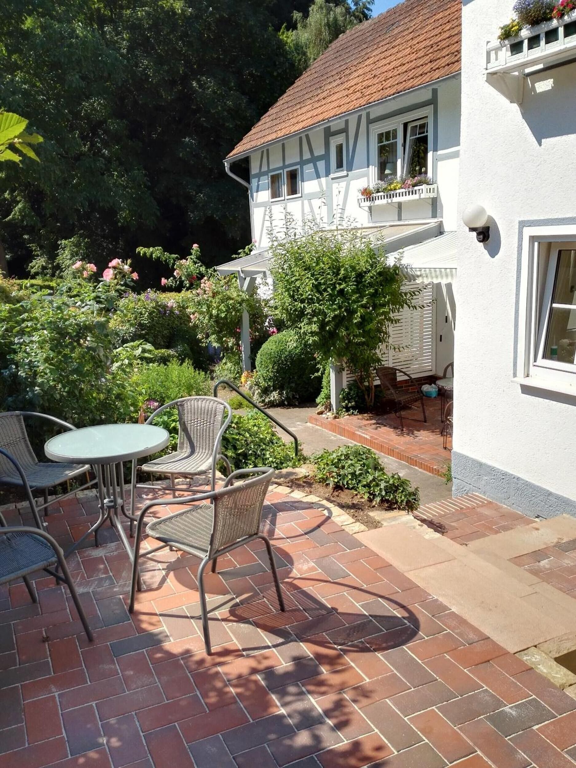 Eine Terrasse mit Korbmöbeln, einem Backsteinweg und einem weißen Gebäude mit Balkon.