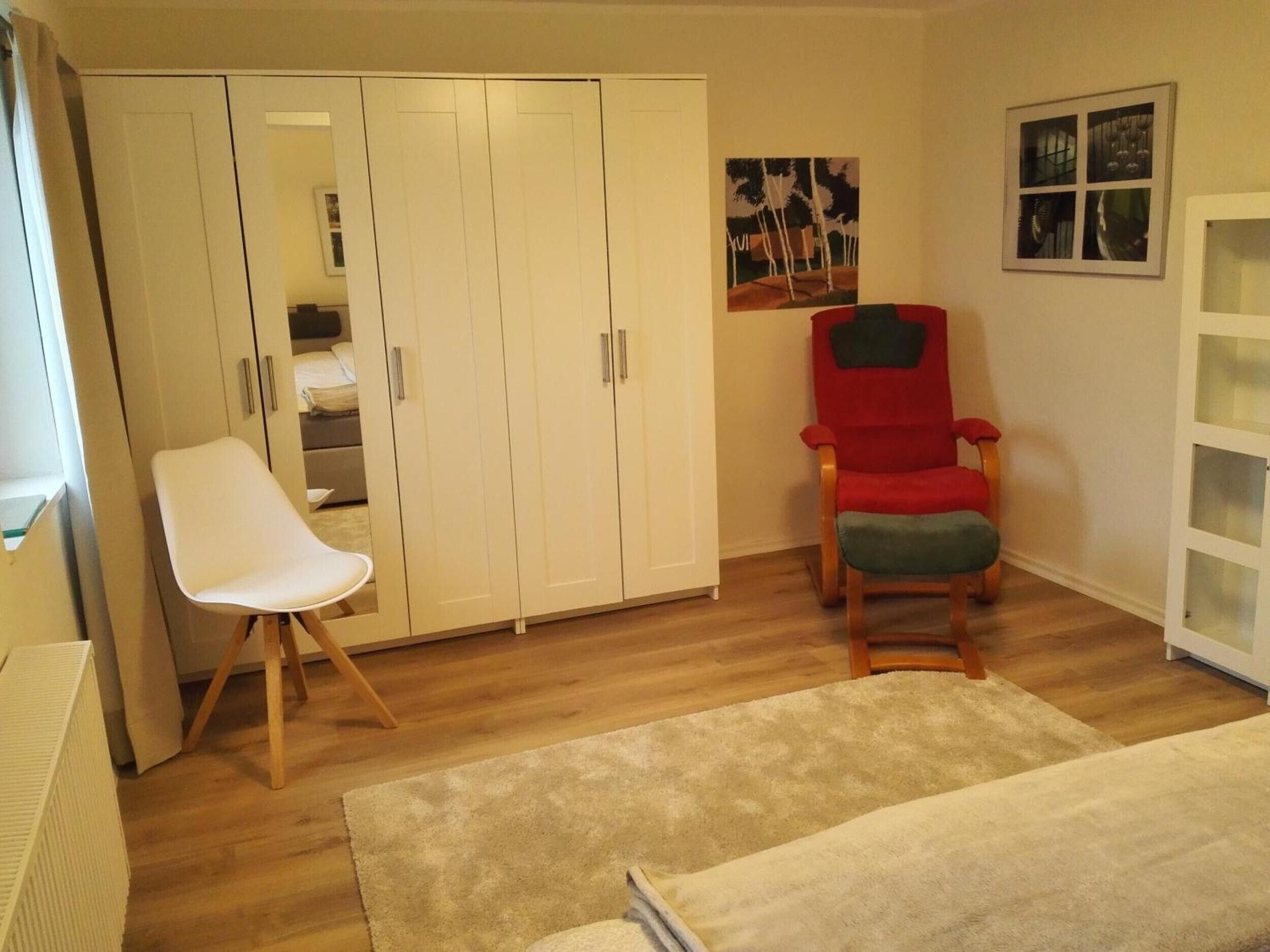 Una habitación con un armario blanco, una silla roja, una silla blanca y una alfombra beige.