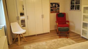Una habitación con un armario blanco, una silla roja, una silla blanca y una alfombra beige.
