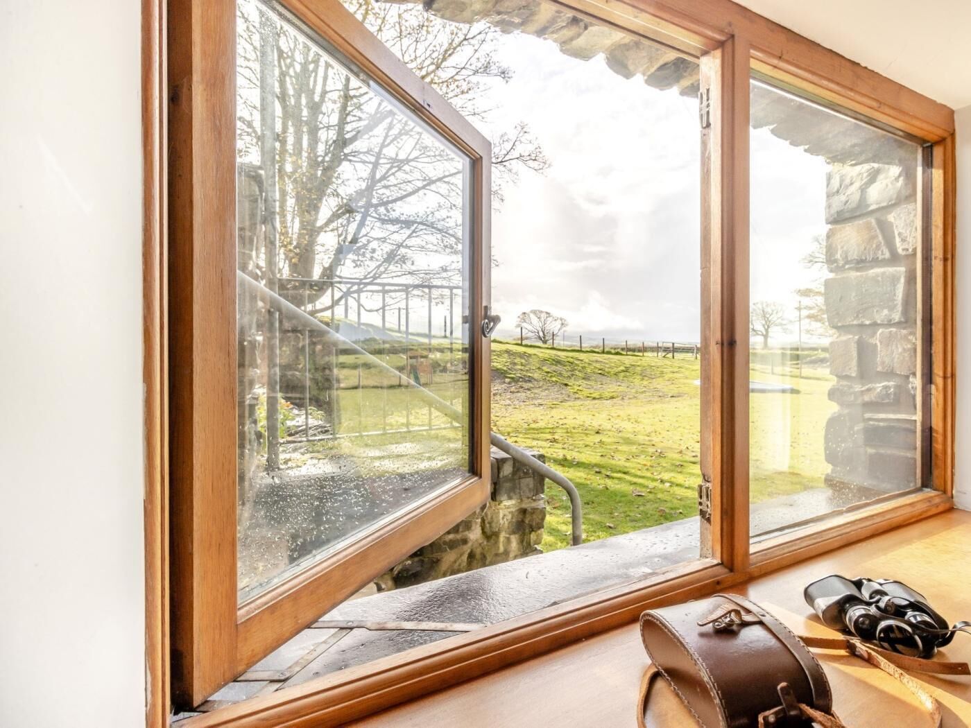 A room with a large window overlooking a grassy area and stone wall.