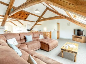 Ein großzügiges Loft mit freiliegenden Holzbalken, einem großen Ecksofa, einem Holztisch und einem Fernseher auf einem Holzboden.