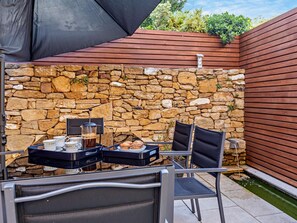An outdoor patio with stone walls, a table with chairs, and a coffee maker.