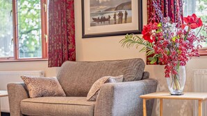 Ein graues Sofa mit passendem Armteil, ein kleiner Holztisch und eine Vase mit roten Blumen.