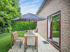 An outdoor patio with a table and chairs, a large umbrella, and a brick wall. - 2 Bed in Christchurch (oc-91999) (Burton)