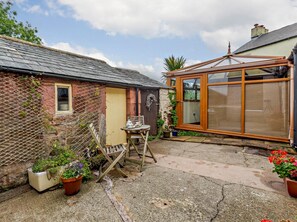 Ein Backsteinhaus mit Holztür, einem Fenster und einem Gartenbereich mit Blumentöpfen und einem Tisch.