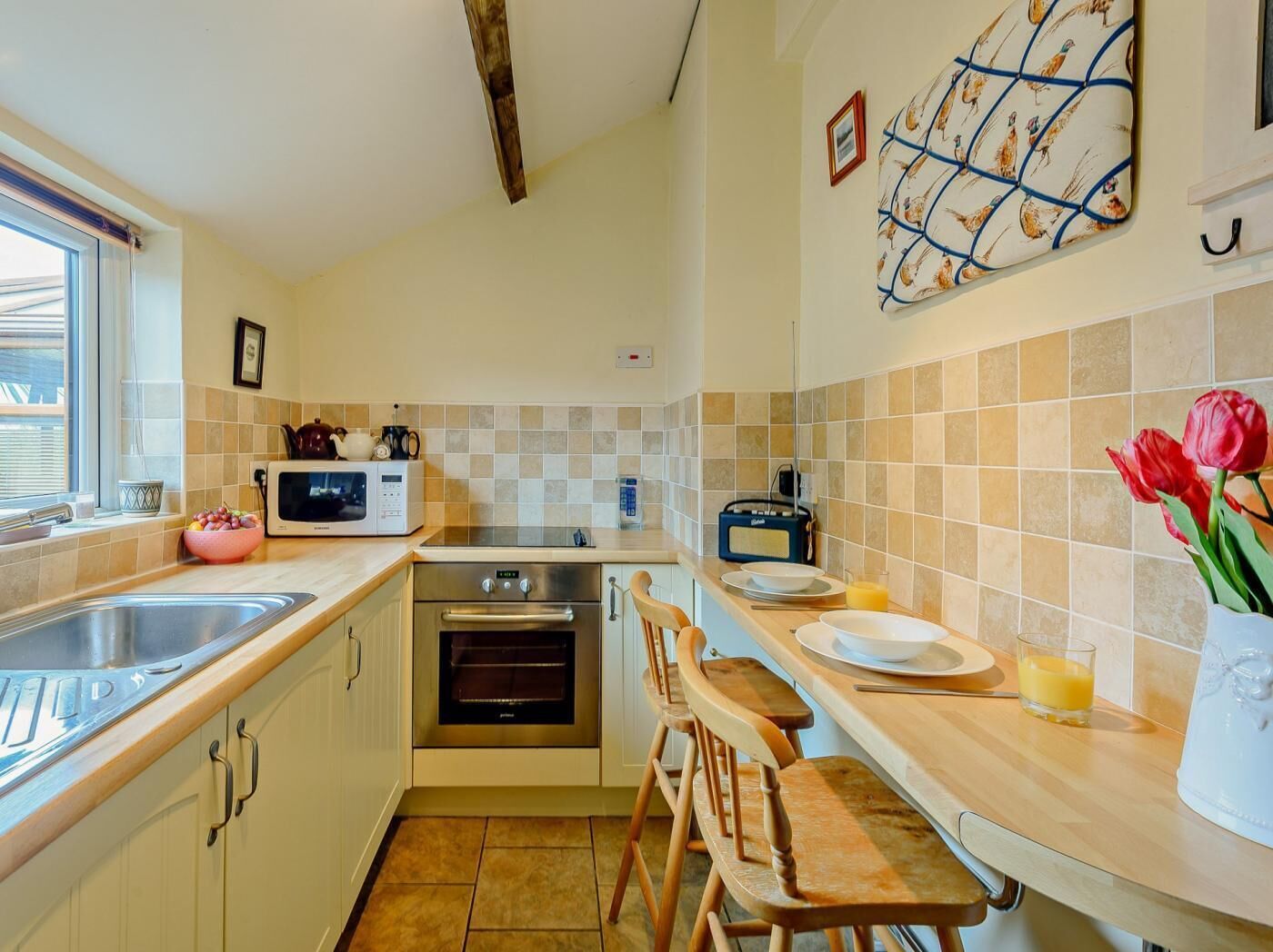 A compact kitchen with a microwave, oven, and a small dining area with wooden chairs.