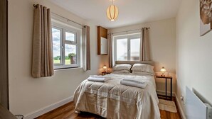Ett sovrum med en stor säng, två sängbord, en hängande lampa och två fönster med gardiner.