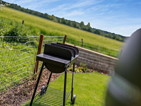 A portable grill set up on a grassy area with a fence and trees in the background. - 2 Bed in Ripon (oc-91955) (West Tanfield)
