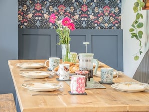 Ein Frühstückstisch mit Tellern, einer Kaffeekanne, einer Blumenvase und einer Dekoration an der Wand.