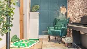 Una stanza con un pianoforte, una poltrona in velluto verde, una scacchiera e una grande decorazione a foglia verde.