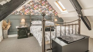 Una camera da letto con soffitto spiovente, un letto con testiera fiorita, un comodino con lampada e una piccola finestra.