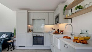 Eine kleine Küche mit weißen Schränken, einer Mikrowelle, einem Spülbecken und einer Frühstücksecke mit Croissants und Orangensaft.