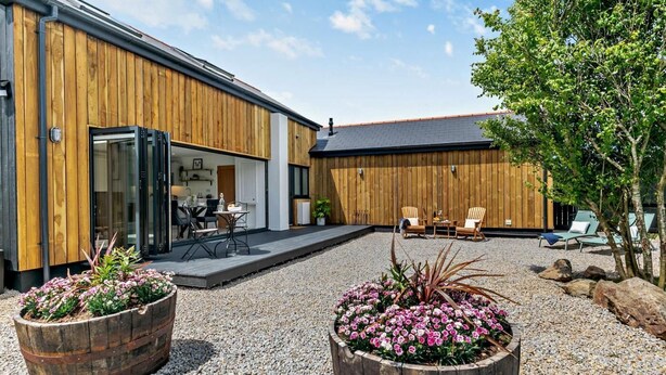 Ein modernes Gebäude mit Holzfassade, einer überdachten Terrasse, Sitzgelegenheiten im Freien und zwei großen Blumenkästen.