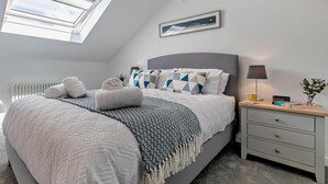Ein Schlafzimmer mit Oberlicht, einem Bett mit gemusterten Bettbezügen, einem Nachttisch mit Lampe und einem gerahmten Bild an der Wand.