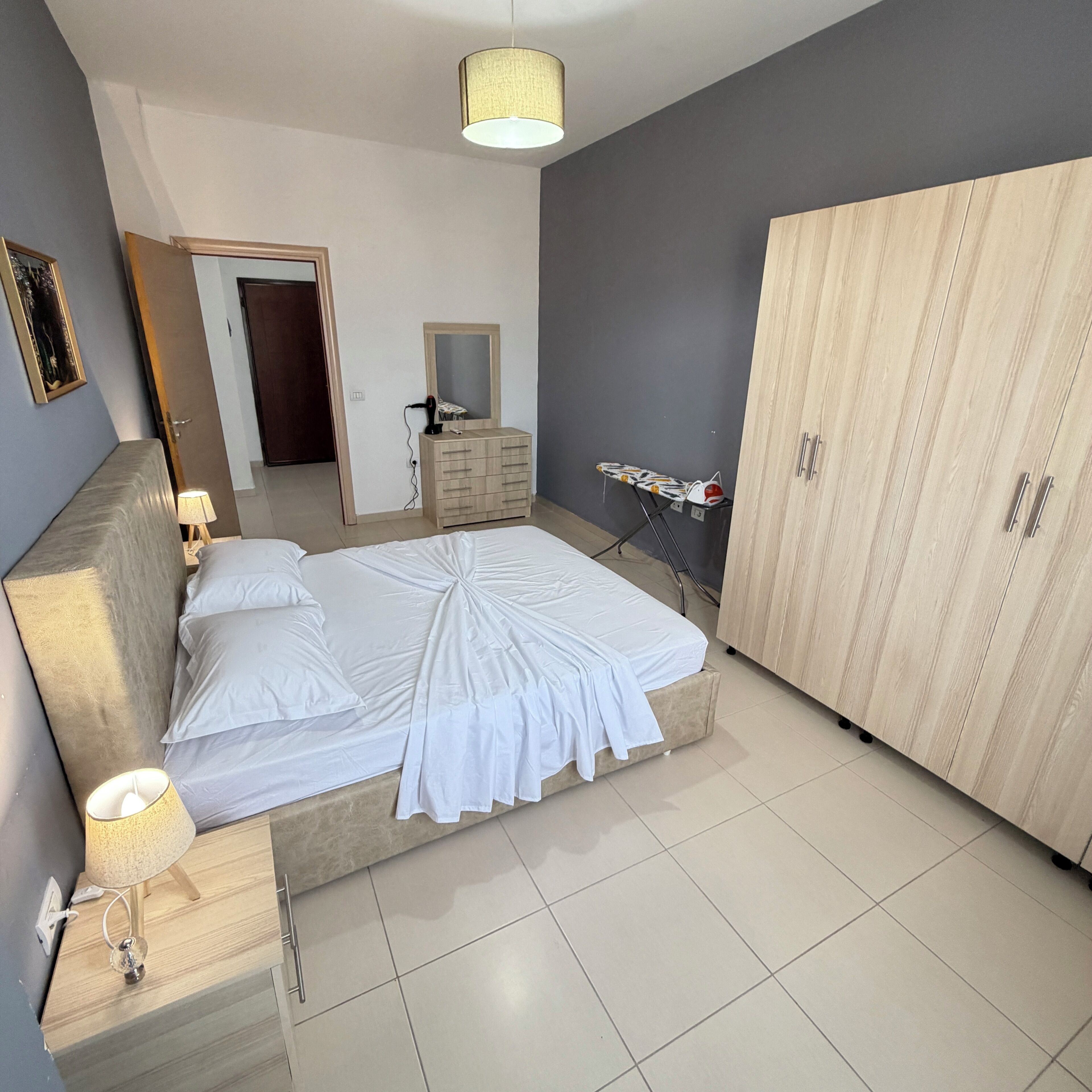 A bedroom with a bed, bedside lamps, a wardrobe, and a mirror.