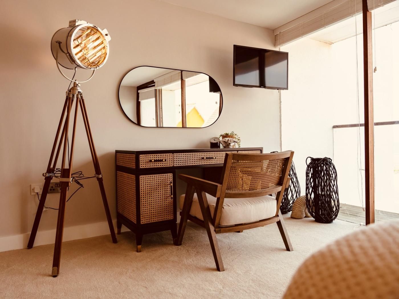 A room with a desk, chair, mirror, and a floor lamp.