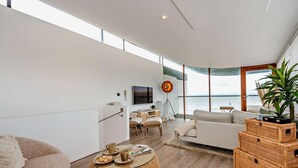 Een moderne woonkamer met een groot raam, een flatscreen televisie en uitzicht op zee.
