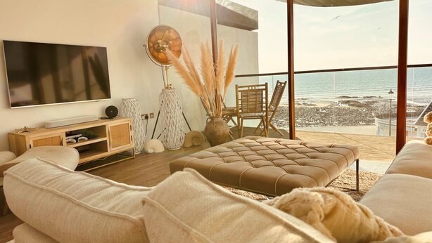Een moderne woonkamer met een grote flatscreen-tv, een comfortabele bank, een salontafel en uitzicht op het strand.