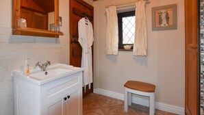 Een badkamer met een witte wastafel, houten kastjes, een witte badjas, een raam met gordijnen en een klein krukje.
