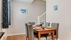 Un comedor con una mesa de madera, sillas tapizadas en gris y una escalera al fondo.