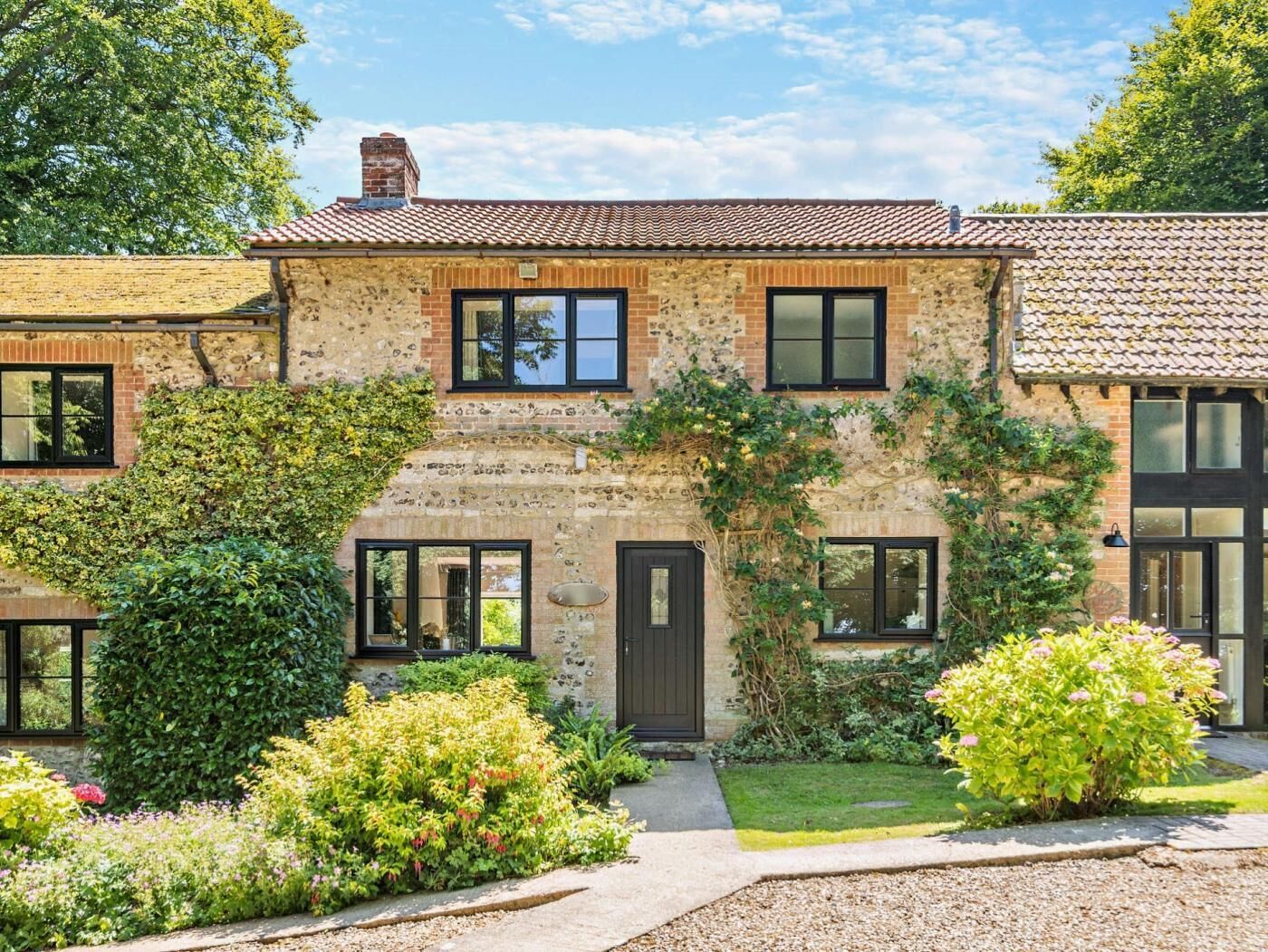 A stone house with a tiled roof, a front door, and a garden with various plants and flowers.