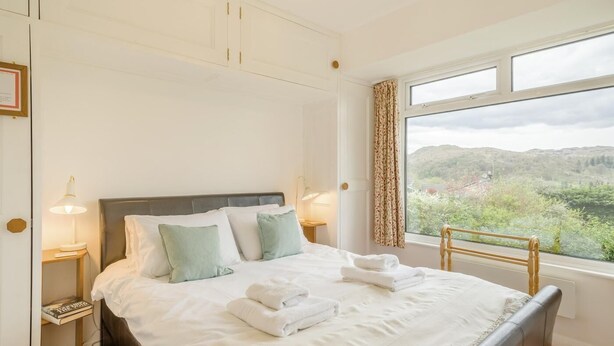 Una cama bien hecha con almohadas, una mesita de noche con lámpara y una ventana con vista a la vegetación.