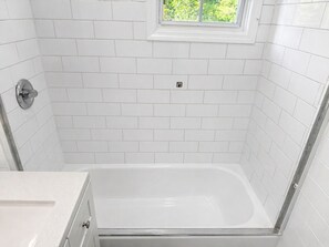 Ein Badezimmer mit weißen Fliesen, einer Badewanne und einem Fenster.