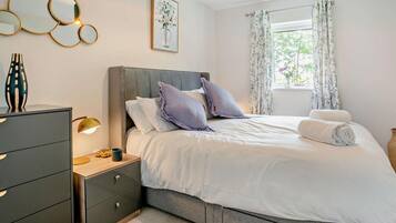Une chambre à coucher comprenant un lit, des tables de chevet, une commode, une lampe, une fenêtre avec des rideaux et des œuvres d’art murales.