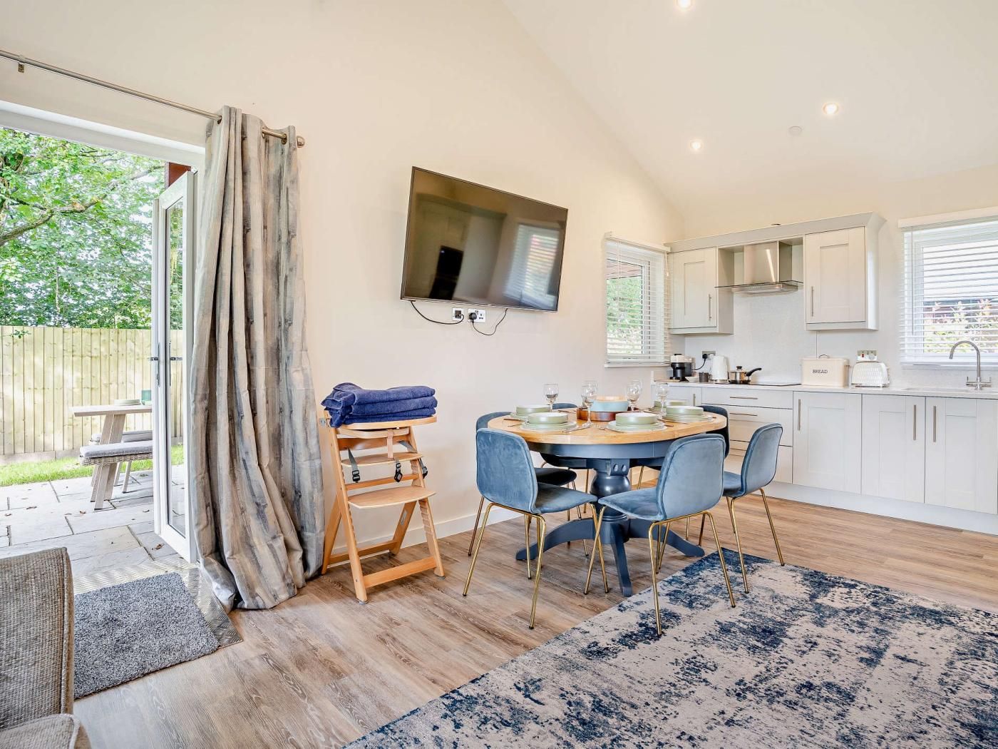 A modern kitchen with a dining area, wooden flooring, and a large window.