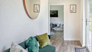 A modern living room with a green sofa, a round mirror, and framed floral artwork on the walls.