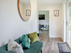 A modern living room with a green sofa, a round mirror, and framed floral artwork on the walls. - 2 Bed in Swansea (oc-91728) (Upper Killay)
