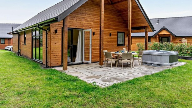 Eine Holzjagdhuette mit überdachter Terrasse, Whirlpool und Essbereich.