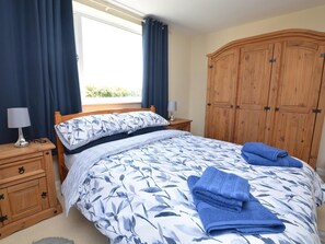 Um quarto com uma cama, um guarda-roupa de madeira, uma mesa de cabeceira com abajur e uma janela com cortinas.